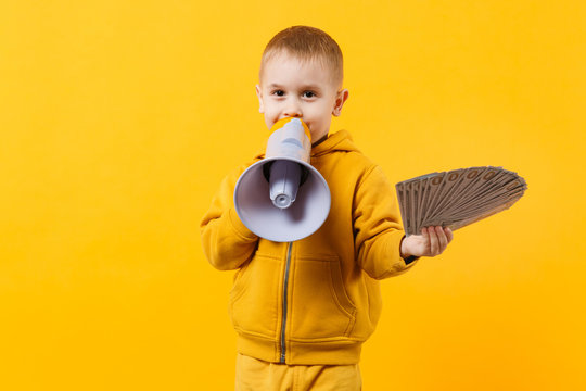 Little happy kid boy in yellow clothes hold fan of money in dollar banknotes, megaphone isolated on orange wall background, children studio portrait. Childhood lifestyle concept. Mock up copy space.