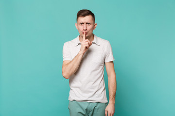 Young man in casual clothes saying hush be quiet with finger on lips shhh gesture isolated on blue turquoise wall background in studio. People sincere emotions, lifestyle concept. Mock up copy space.