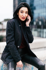 Attractive young woman is speaking on the phone and laughing sincerely over grey street stairs background