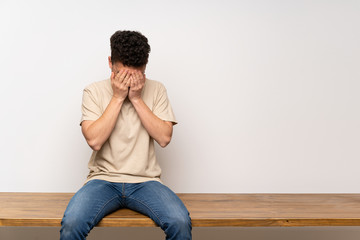 Young man sitting on table with tired and sick expression