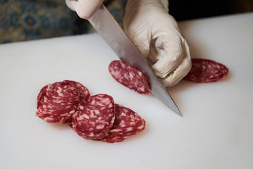 Men's hands cut sausage salami on a white cutting board, close-up