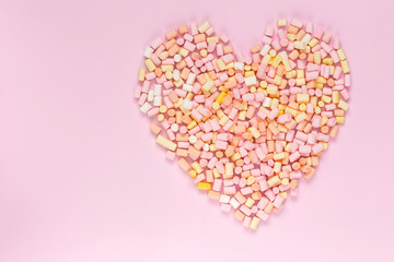 Top view of the multi-colored marshmallows which lies in the shape of a heart on a monochrome pink background copyspace, topview, mockup, flatlay