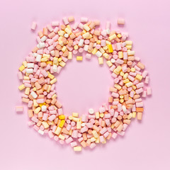 Top view of the multi-colored marshmallows which lies in the shape of a round frame with an area for text in the center on a monochrome pink background