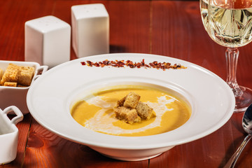 Spicy Pumpkin or lentil soup with cream an croutons in white plate on wooden background