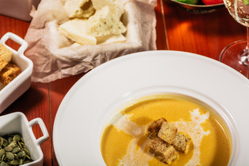 Dietary vegetarian pumpkin cream soup puree, served with white wine, pumpkin seeds, cheese and croutons, on brown wooden table, close up.