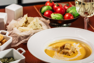 Roasted pumpkin and carrot soup with cream, pumpkin seeds. Served with croutons, cheese and white wine on wooden background. Copy space