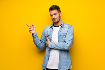 Handsome man over yellow wall pointing finger to the side