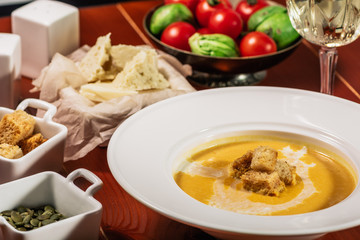 Roasted pumpkin and carrot soup with cream, pumpkin seeds. Served with croutons, cheese and white wine on wooden background. Copy space