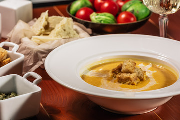 Roasted pumpkin and carrot soup with cream, pumpkin seeds. Served with croutons, cheese and white wine on wooden background. Copy space