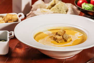 Dietary vegetarian pumpkin cream soup puree, served with white wine, pumpkin seeds, cheese and croutons, on brown wooden table, close up.