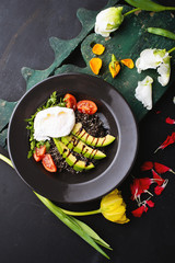 Healthy salad served in dark plate, avocado, tomatoes, sour cream and rucola, surrounded by tulips