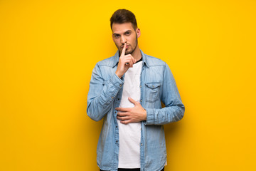 Handsome man over yellow wall showing a sign of silence gesture putting finger in mouth