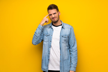 Handsome man over yellow wall making the gesture of madness putting finger on the head