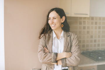 Attractive young woman smiling and looking away with crossed hnads in  her kitchen at home