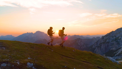 AERIAL: Flying along a cheerful couple hiking down a grassy hill in the Alps.