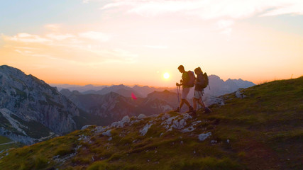 LENS FLARE: Active woman and boyfriend descending down the mountain at sunrise.