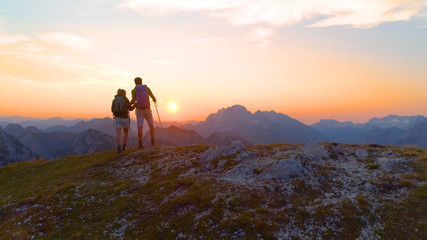 AERIAL: Unrecognizable hiker couple observes evening landscape from mountaintop.