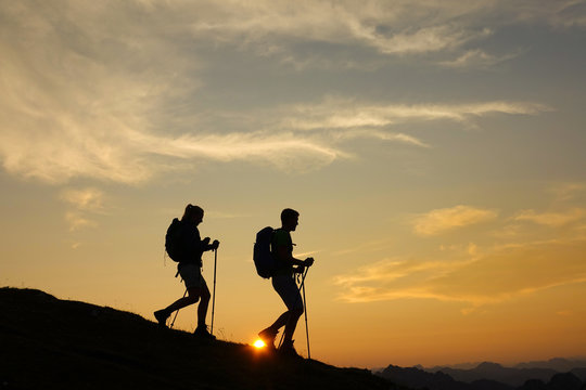 SILHOUETTE: Active tourists are hiking down a grassy hill in the peaceful Alps.