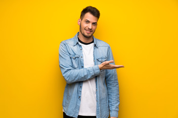 Handsome man over yellow wall presenting an idea while looking smiling towards