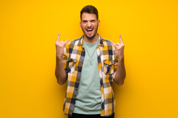 Handsome man over yellow wall making rock gesture - obrazy, fototapety, plakaty