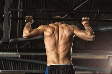 Fototapeta na wymiar Back muscles. Rearview shot of a shirtless man with toned muscular body working out doing pull-ups at the gym sports athlete activity lifestyle health muscles strength motivation endurance concept