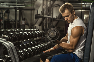 Feel the biceps burn. Muscular young man working out at the gym doing biceps curls with dumbbells...