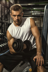Fototapeta na wymiar Intense training. Vertical shot of a serious young handsome man looking to the camera fiercely lifting weights at the gym dumbbells iron pump muscular body biceps sports motivation lifestyle concept