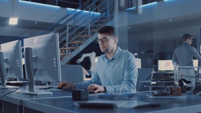Electronics Development Engineer Sitting at His Desk Uses personal Computer for Programming. Team of Professionals Use Digital Whiteboard with CAD Software for the Modern Industrial Engineering Design