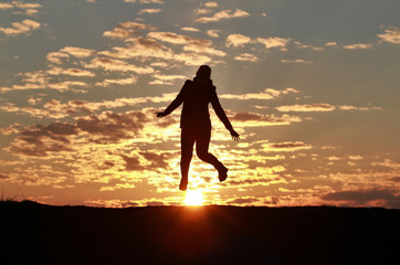 Silhouette of a happy girl jumping into the sky against the backdrop of an incredible sunset, sky and clouds