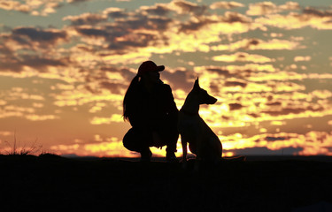 Fototapeta na wymiar Silhouette of a girl and dogs against the backdrop of an incredible sunset, sky and clouds. Belgian Shepherd Malinois