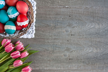Wielkanocne tło z różowymi tulipanami i koszykiem pełnym kolorowych pisanek