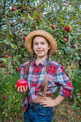 Portrait of a cute girl in a farm garden with a red apple.