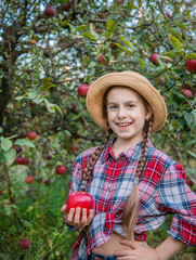 Portrait of a cute girl in a farm garden with a red apple.