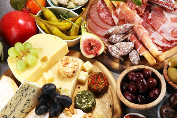 Italian antipasti wine snacks set. Cheese variety, Mediterranean olives, crudo, Prosciutto di Parma, salami and wine in glasses over grunge background.