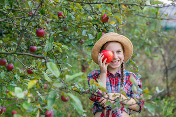 Portrait of a cute girl in a farm garden with a red apple.