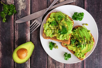 Avocado toasts with pumpkin and chia seeds on whole grain bread. Above view on a dark wood...