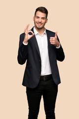 Handsome business man showing ok sign with and giving a thumb up gesture over ocher background