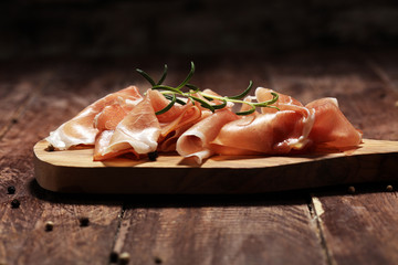 Italian prosciutto crudo or jamon with rosemary. Raw ham on rustic background