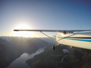 Small airplane flying near the rocky Canadian Mountains during a vibrant summer sunset. Taken near Squamish, North of Vancouver, British Columbia, Canada.