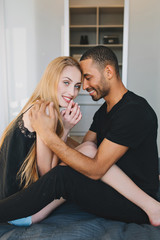 Lovely couple moments of handsome guy caring at young pretty woman with long blonde hair, hugging her on bed in modern apartment.  Chilling together in the morning, love, relationship