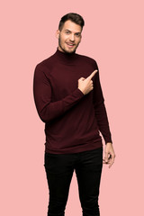 Man with turtleneck sweater surprised and pointing finger to the side over pink background