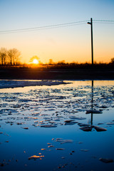 Spring landscape. A flood on the street at sunset. Reflection on the water. Ice fragments close-up....
