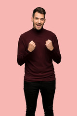 Man with turtleneck sweater celebrating a victory in winner position over pink background