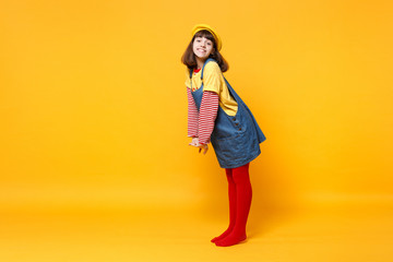 Full length portrait of beautiful girl teenager in french beret and denim sundress standing isolated on yellow wall background in studio. People sincere emotions lifestyle concept. Mock up copy space.