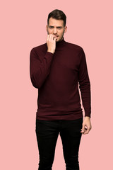 Man with turtleneck sweater nervous and scared putting hands to mouth over pink background