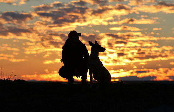 Silhouette of a girl and dogs against the backdrop of an incredible sunset, sky and clouds. Belgian Shepherd Malinois