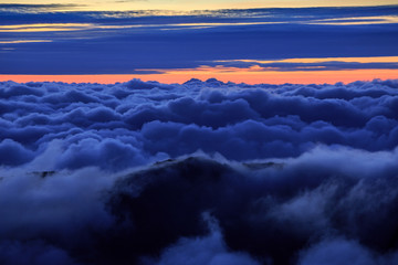 Abstract photograph above the clouds, sea of clouds effect, flying through the sky, aerial view, puffy clouds, orange sunset sky. Low pressure front atmospheric effect, cloudscape, clear weather.