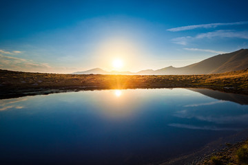 Mountain lake landscape at sunset with sun reflection scenic view