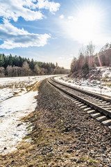 Railway passes through a spring forest, melting snow from the rays of the spring sun, sunny day with blue sky and clouds