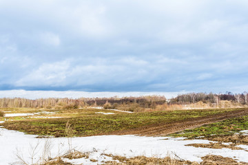 The melting of the snow on the fields in early spring, sunny day with blue sky and clouds